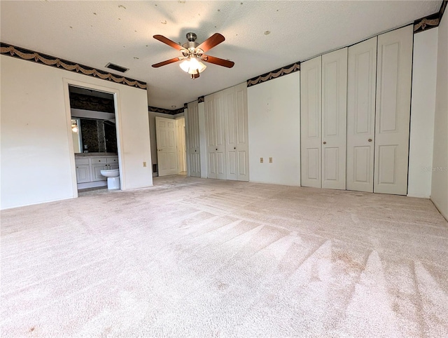 unfurnished bedroom featuring light carpet, two closets, ceiling fan, a textured ceiling, and connected bathroom