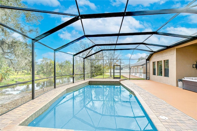 outdoor pool featuring glass enclosure, a patio, and a water view