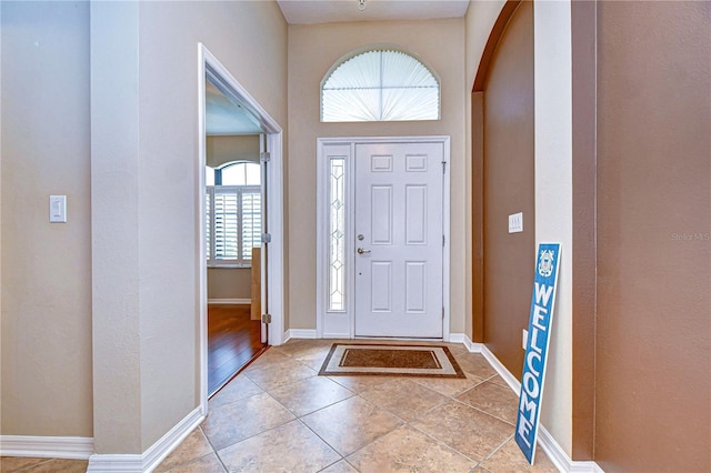 foyer featuring baseboards, arched walkways, and light tile patterned flooring