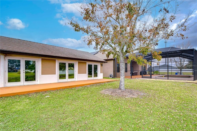 rear view of house with stucco siding, a lawn, french doors, roof with shingles, and a lanai