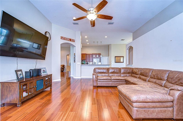 living room with arched walkways, a ceiling fan, visible vents, and light wood-type flooring