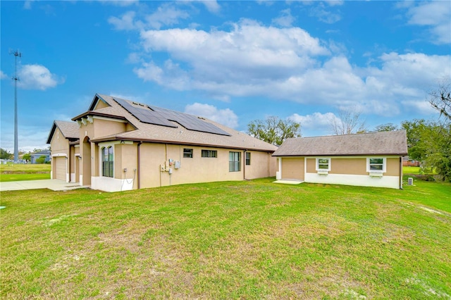 back of property with roof mounted solar panels, driveway, stucco siding, and a lawn