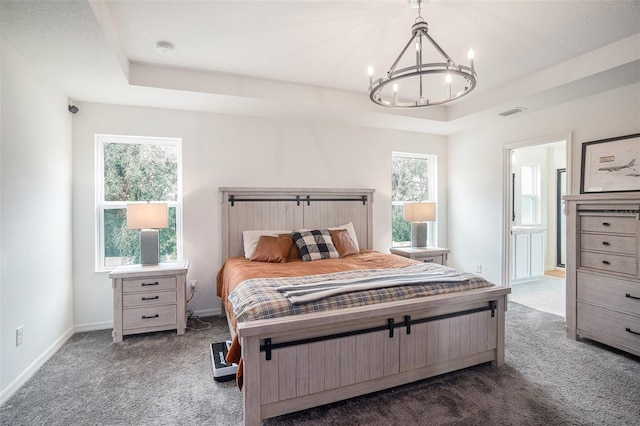 bedroom with dark carpet, connected bathroom, an inviting chandelier, and a raised ceiling