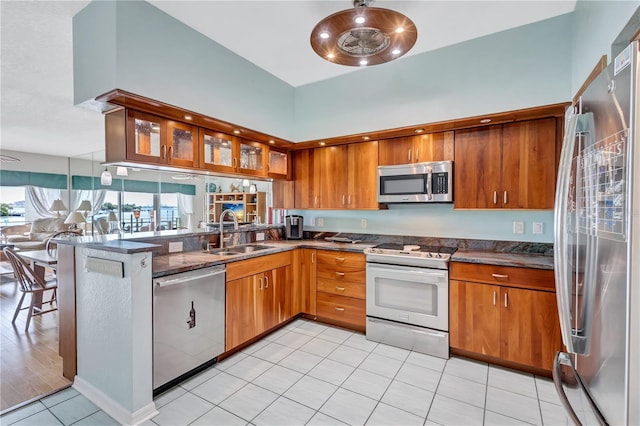 kitchen with sink, kitchen peninsula, dark stone counters, light tile patterned flooring, and appliances with stainless steel finishes