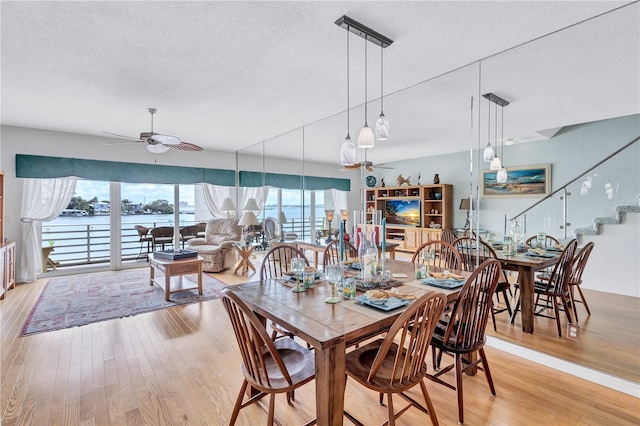 dining space featuring ceiling fan, a water view, light hardwood / wood-style floors, and a textured ceiling