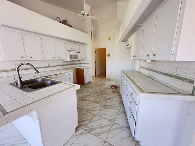 kitchen with tile counters, sink, a towering ceiling, white appliances, and white cabinets