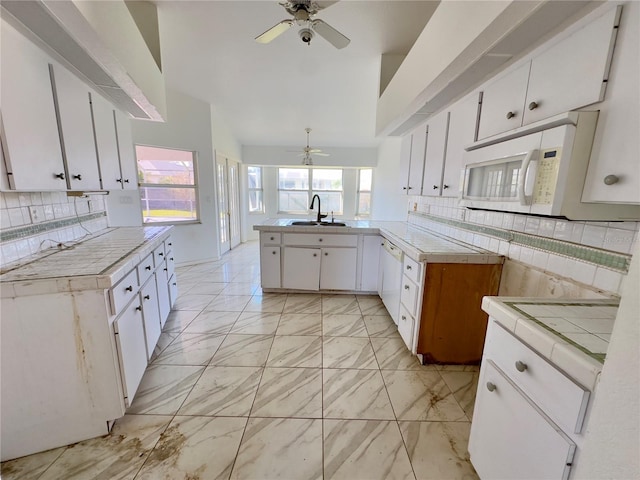 kitchen featuring tile countertops, white appliances, sink, white cabinetry, and kitchen peninsula