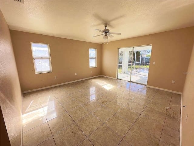 empty room featuring light tile patterned floors, a textured ceiling, a wealth of natural light, and ceiling fan