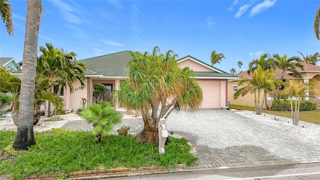 view of property hidden behind natural elements with a garage, decorative driveway, a tiled roof, and stucco siding