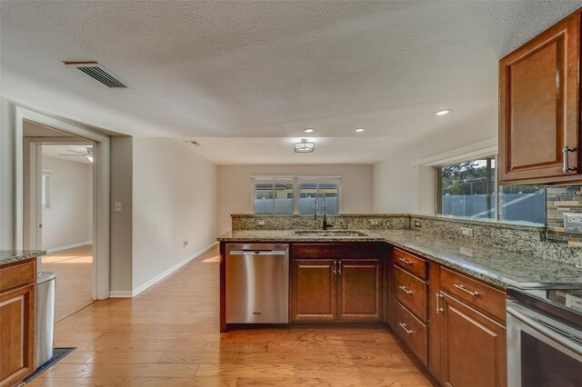 kitchen featuring light stone counters, dishwasher, light wood-type flooring, and sink