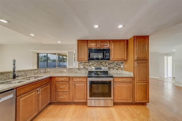 kitchen featuring light stone countertops, sink, stainless steel appliances, tasteful backsplash, and light wood-type flooring