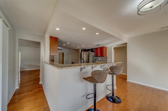 kitchen with tasteful backsplash, light hardwood / wood-style flooring, kitchen peninsula, stainless steel fridge, and a breakfast bar