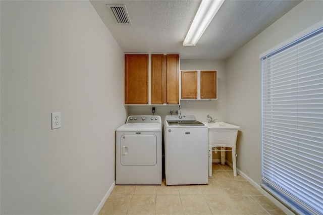 clothes washing area featuring cabinets, independent washer and dryer, a textured ceiling, and light tile patterned floors