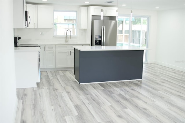 kitchen featuring sink, decorative light fixtures, stainless steel fridge with ice dispenser, a center island, and white cabinetry