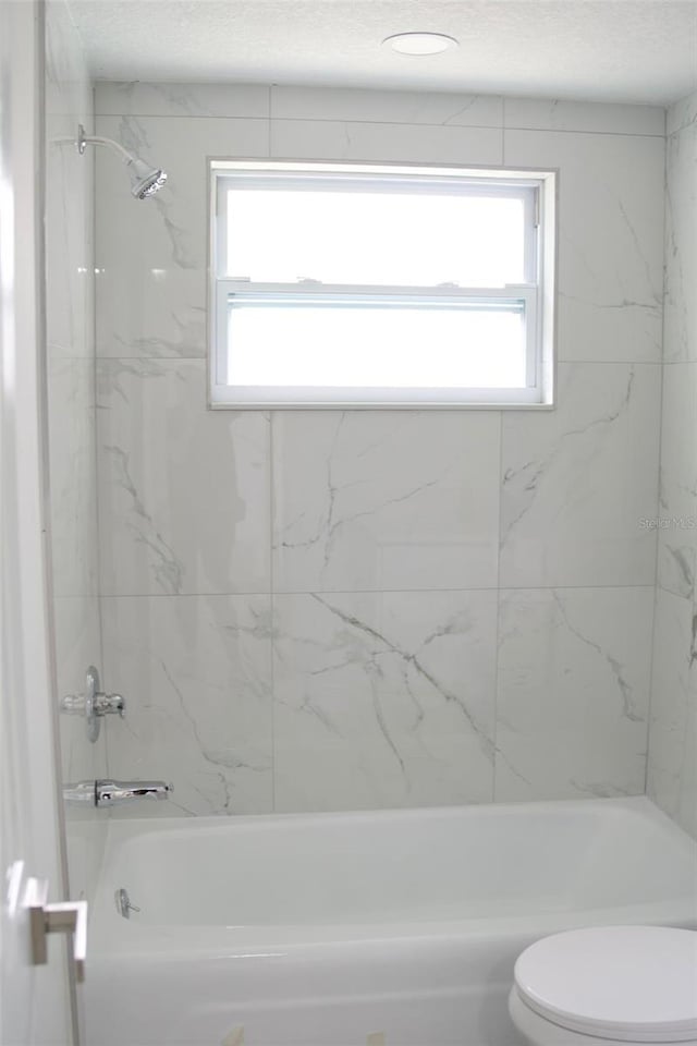 bathroom featuring tiled shower / bath combo and toilet