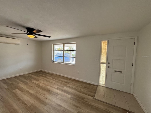 entrance foyer with ceiling fan, light wood-type flooring, an AC wall unit, and a textured ceiling