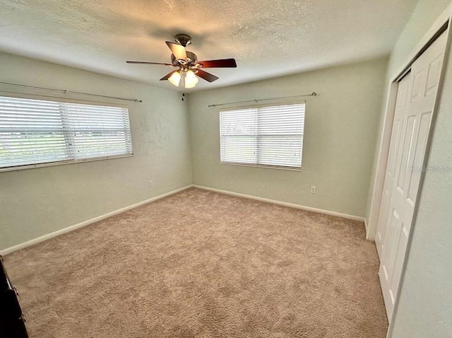 unfurnished bedroom featuring light carpet, a textured ceiling, a closet, and ceiling fan