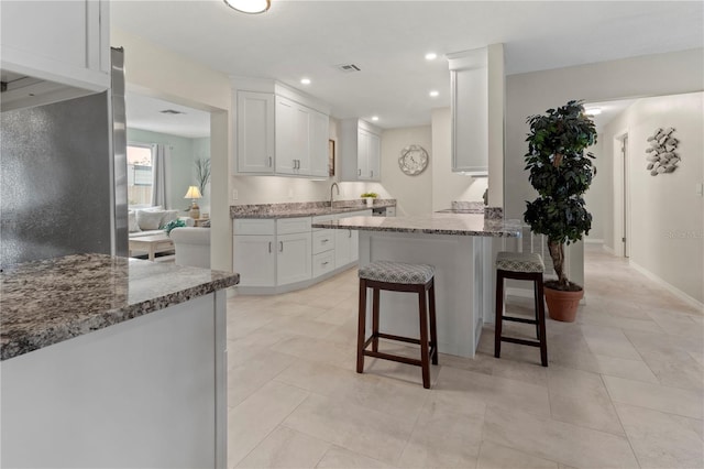 kitchen featuring a kitchen breakfast bar, sink, kitchen peninsula, stone countertops, and white cabinetry