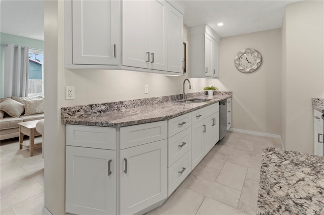 kitchen featuring light stone countertops, stainless steel dishwasher, sink, light tile patterned floors, and white cabinetry