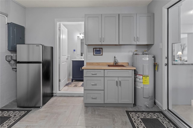 kitchen with electric panel, sink, gray cabinets, water heater, and stainless steel refrigerator