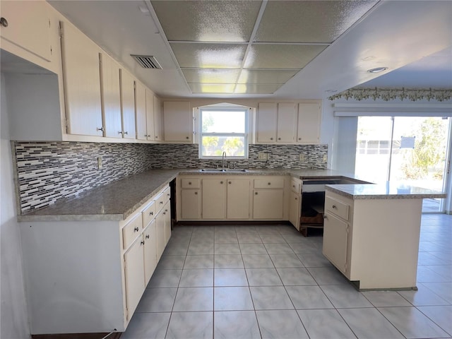 kitchen with cream cabinetry, kitchen peninsula, light tile patterned floors, sink, and backsplash