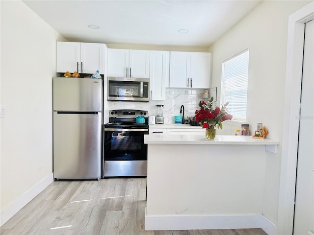 kitchen featuring white cabinetry, sink, backsplash, appliances with stainless steel finishes, and light wood-type flooring