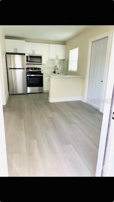 kitchen with white cabinets, backsplash, light hardwood / wood-style floors, and stainless steel appliances