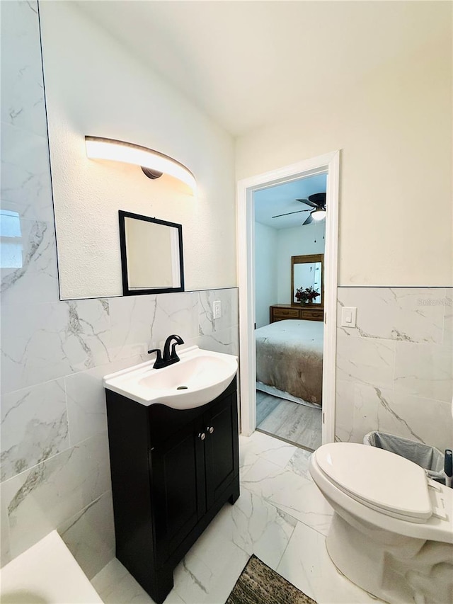 bathroom with ceiling fan, vanity, tile walls, and toilet