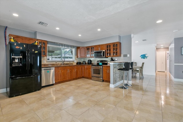 kitchen featuring sink, kitchen peninsula, a textured ceiling, a breakfast bar area, and appliances with stainless steel finishes