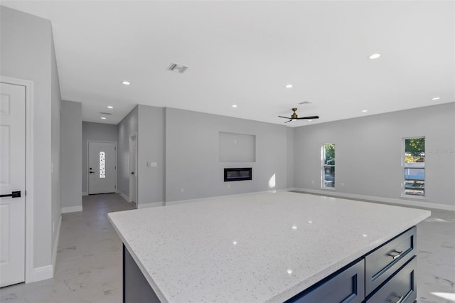 kitchen with ceiling fan, a center island, and light stone counters