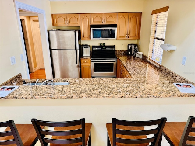 kitchen featuring sink, a breakfast bar area, kitchen peninsula, stainless steel appliances, and light stone countertops