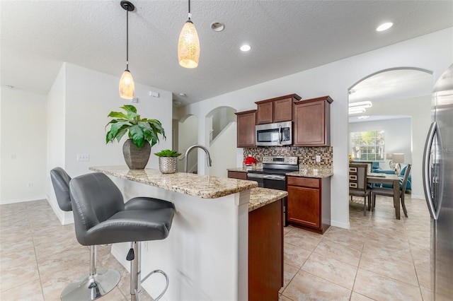 kitchen featuring light stone countertops, appliances with stainless steel finishes, decorative light fixtures, and tasteful backsplash