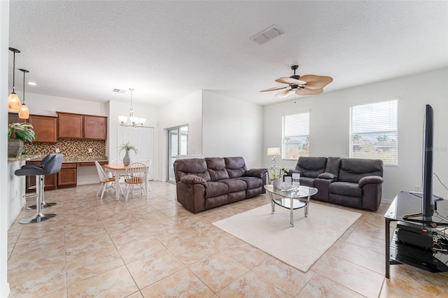 tiled living room with ceiling fan with notable chandelier and a textured ceiling