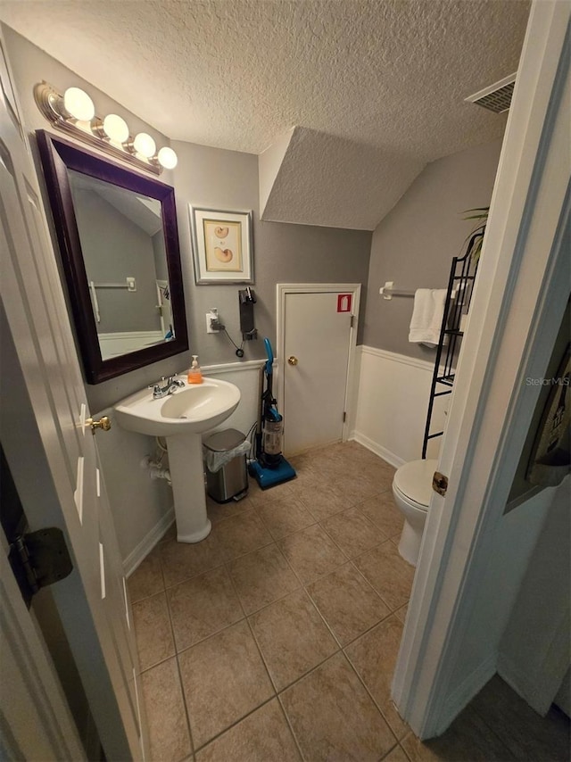 bathroom with vaulted ceiling, tile patterned floors, a textured ceiling, and toilet