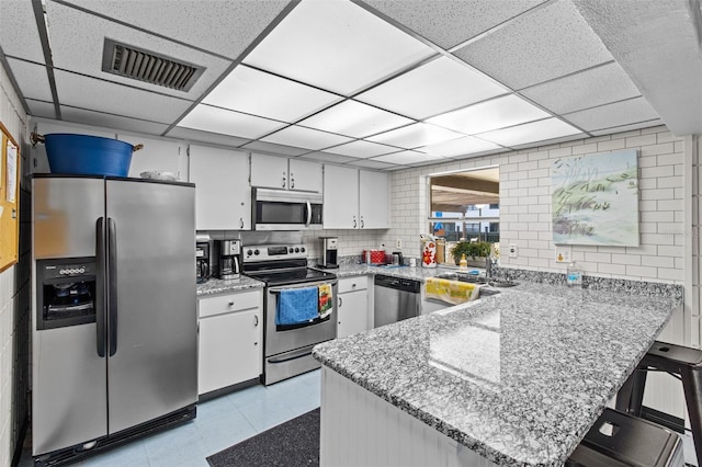 kitchen featuring a drop ceiling, stainless steel appliances, kitchen peninsula, and white cabinets