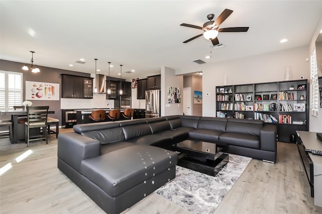 living room featuring ceiling fan with notable chandelier and light hardwood / wood-style flooring