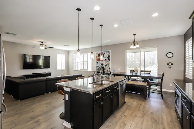 kitchen with a kitchen island with sink, ceiling fan with notable chandelier, sink, decorative light fixtures, and light hardwood / wood-style floors