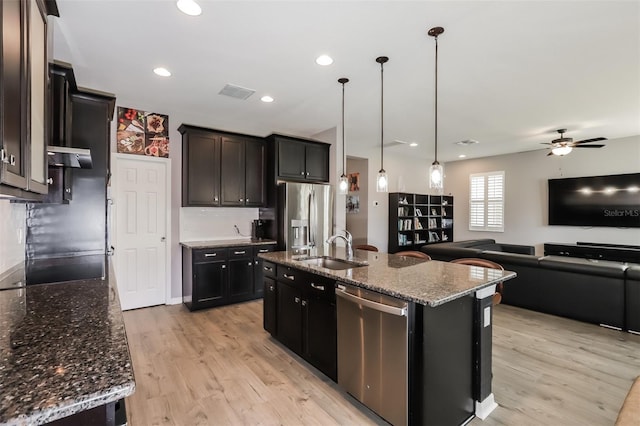 kitchen featuring ceiling fan, sink, hanging light fixtures, stainless steel appliances, and a center island with sink