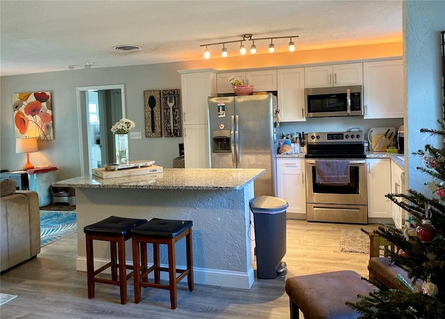 6951 S Shore Dr S, South Pasadena, FL 33707 - kitchen featuring light wood finished floors, white cabinets, light stone countertops, a kitchen island, and appliances with stainless steel finishes