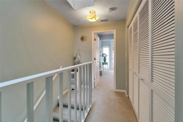 hall featuring a textured ceiling, a skylight, and light colored carpet