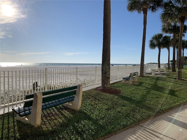 view of property's community with a lawn, a water view, and a view of the beach