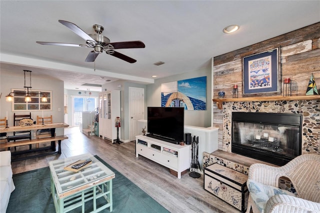 living room with wood-type flooring, a stone fireplace, and ceiling fan