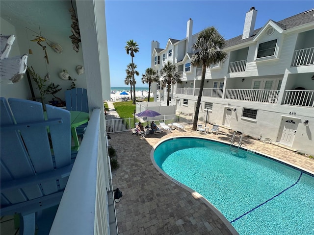 community pool with a fenced backyard, a beach view, a water view, and a patio area