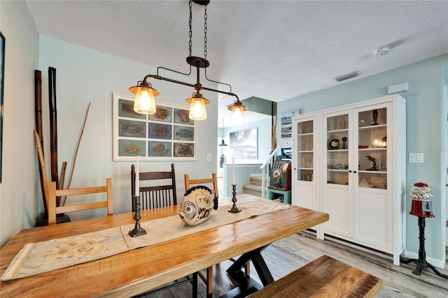 dining room featuring visible vents, a textured ceiling, wood finished floors, and stairway