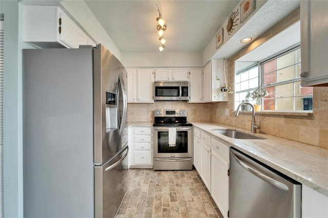 kitchen featuring brick patterned floor, white cabinetry, a sink, appliances with stainless steel finishes, and backsplash