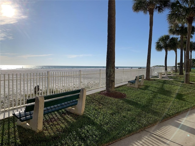 view of property's community featuring a lawn, a water view, a view of the beach, and fence