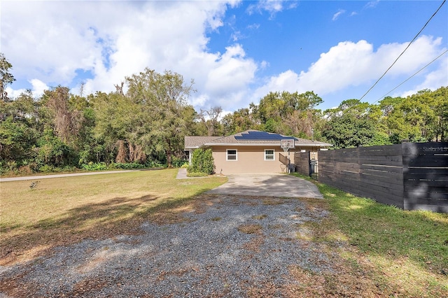 rear view of house with driveway, a lawn, solar panels, fence, and stucco siding