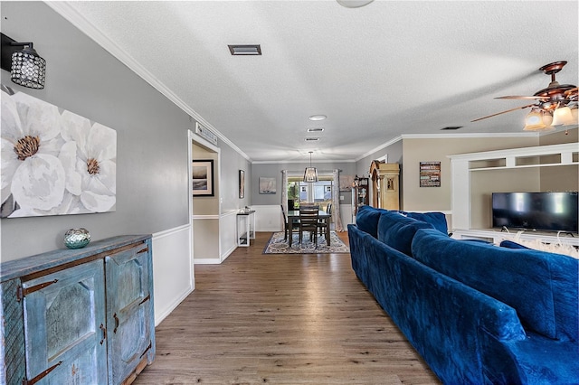 living area featuring ceiling fan, a textured ceiling, ornamental molding, and wood finished floors