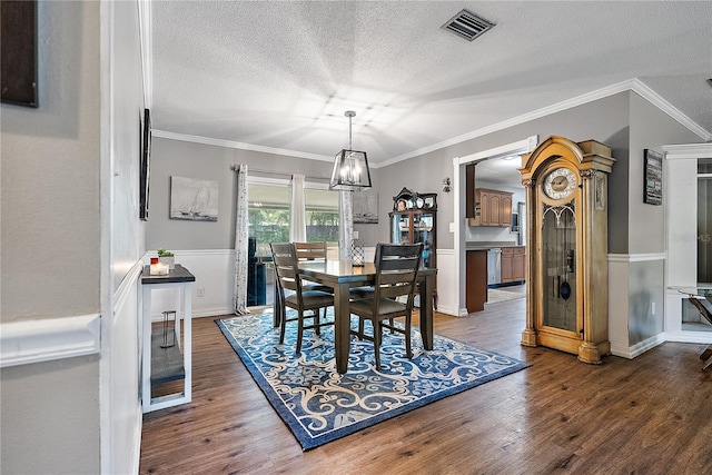 dining space with a wainscoted wall, crown molding, visible vents, dark wood-type flooring, and a textured ceiling