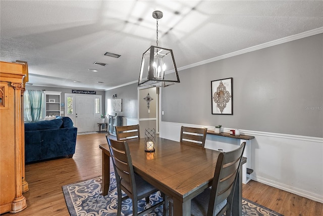 dining space with ornamental molding, visible vents, a textured ceiling, and wood finished floors